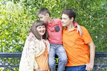 Happy family son kissing pregnant mother in summer embankment