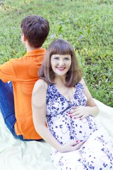 Pregnant wife support of husband back sitting on green grass