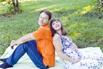 Husband and pregnant wife sitting on green grass in summer time