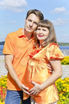 Husband embraces pregnant wife in summer embankment