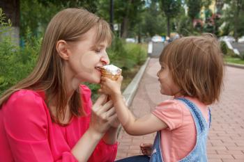 Photo of cute baby girl feeding mother icecream in summer