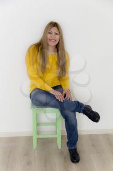 Smiling girl with long brown healthy straight hair in yellow are sitting on the stool