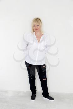 Blond woman in white and black jeans stand inside empty room