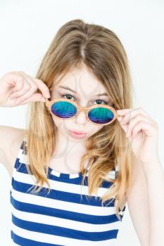Cute blond girl eleven years old standing near white wall with green sunglasses