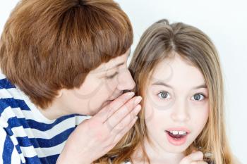Mother says secret an ear her daughter on white wall