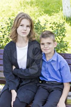 Brother and sister are sitting on bench in summer