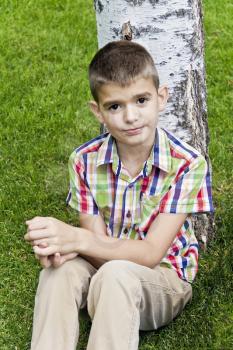 Cute brunette boy eleven years old sitting near tree