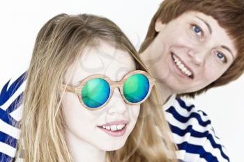 Mother and daughter in green sunglasses playing near white wall