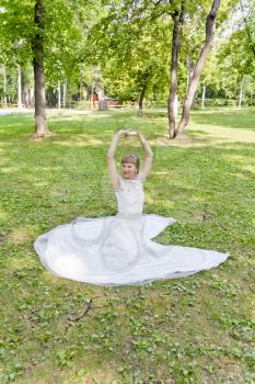 Bride in white lace dress with upwards hands sitting on the grass