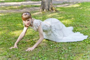 Bride in white lace dress crawl on green grass at the summer time