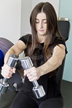 Brunette with long hair do exercise with dumbbells in gym