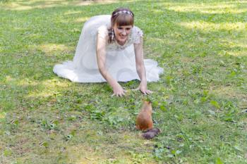 Bride in white lying on green grass next to the squirrel in summer