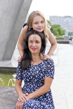 Embracing mother and daughter near fountain in summer time