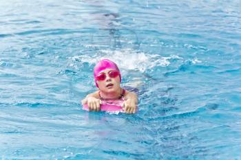 Cute girl with pink rubber hat are swimming in pool