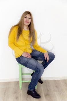 Attractive young girl in yellow are sitting on stool