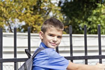 Boy are hanging on the fence with school backpack