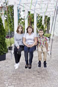 Happiest mother with daughter and son ride on a swing
