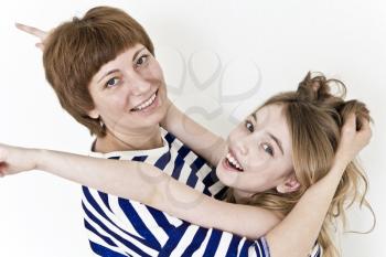 Happiest mother and daughter playing near white wall in striped clothes