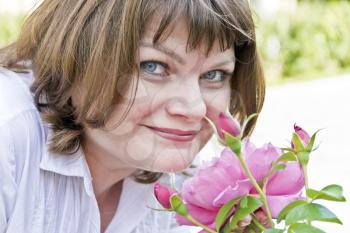Beautiful smiling woman in white are sniffing peonies