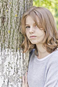 Beautiful girl fourteen years old lean against tree