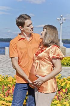 Couple in orange clothers awaiting baby on yellow flowers background