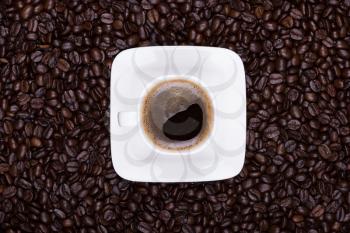 Still-life with coffee cup on scattered coffee beans, top view
