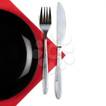 Black plate, fork and knife on red napkin. Isolated on white. Square format.