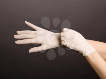 Female hands putting on latex gloves on dark background