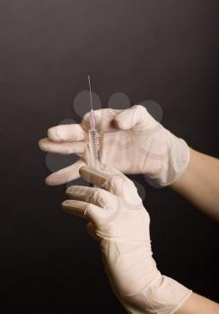 Female hands in latex gloves. Flicking syringe on dark background