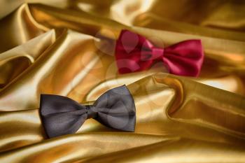 Red and black bow ties on draped golden satin