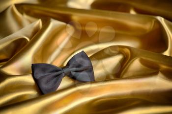 Black bow tie on draped golden satin