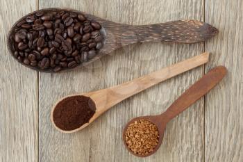 Coffee beans, milled coffee and instant coffee in vintage wooden spoons on a light wooden table.