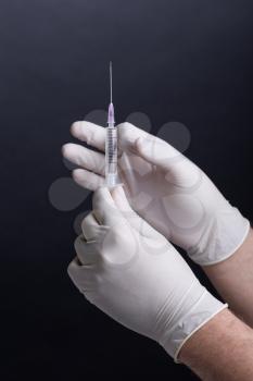 Male hands in latex gloves holding a syringe on dark background