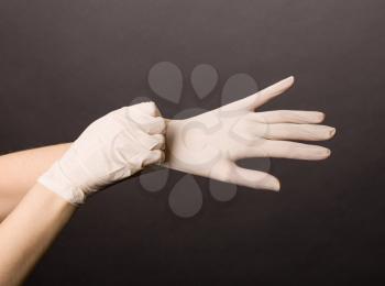 Female hands putting on latex gloves on dark background