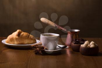 Cup of coffee, turkish pot, croissant, spices, brown sugar and chocolate on a dark background.
