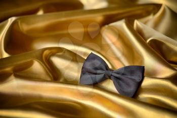 Black bow tie on draped golden satin
