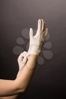 Female hands in golves. Doctor or nurse putting on latex gloves. Sanitary, healthcare, medical clothing. Dark background
