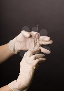 Female hands in latex gloves. Flicking syringe. Doctor or nurse preparing for medical procedure. Dark background