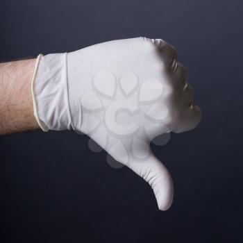 Male hand in latex glove. Thumb down sign. Bad outcome, medical failure, bad healthcare concept. Dark background