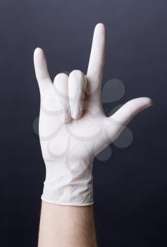 Male hand in latex glove. Doctor or nurse showing a love sign. Dark background