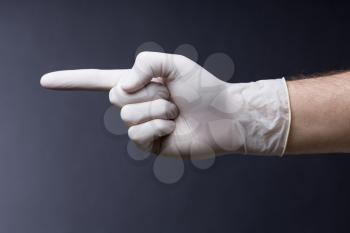 Male hand in latex glove. Doctor or nurse poiting with a finger. Dark background