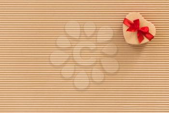 Heart shaped gift box with red ribbon and bow on corrugated cardboard background.