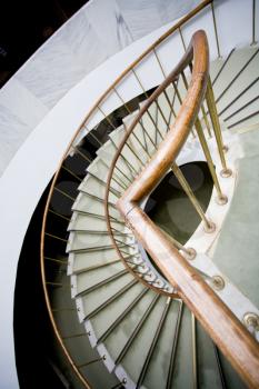 Bended brown wooden handhold of spiral stone stairs