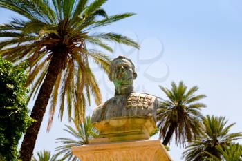 old bronze bust of general under palm trees