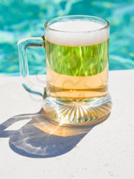 glass of cold beer on pool board in hot summer day 