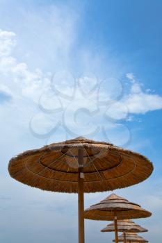 straw parasols and blue sky on San Marco beach near Taormina, Sicily