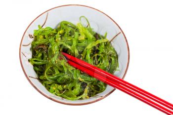 eating of chuka salad - seaweed salad sprinkled with sesame seeds in bowl with red chopsticks isolated on white background