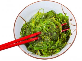 eating of chuka salad - top view of seaweed salad sprinkled with sesame seeds in bowl with red chopsticks isolated on white background