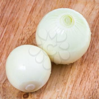 two peeled onions bulbs on wooden cutting board