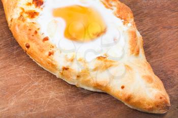 hachapuri by Adzharia (Georgian cheese pastry), filled with cheese and topped with a soft-boiled egg and butter on wooden board close up